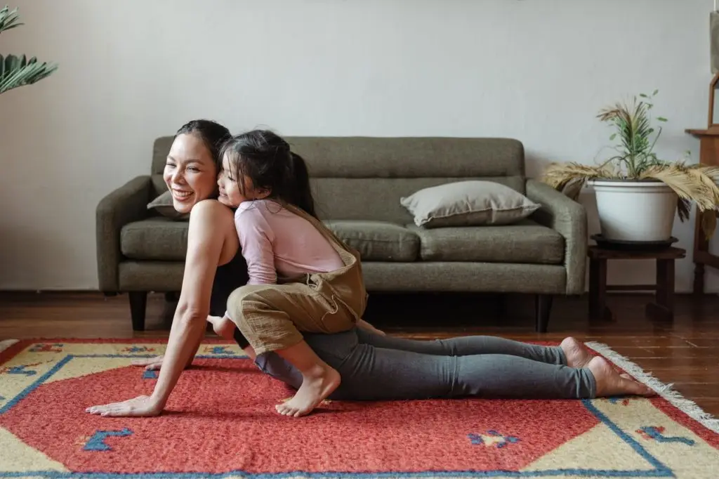 woman doing yoga with child playing on her back